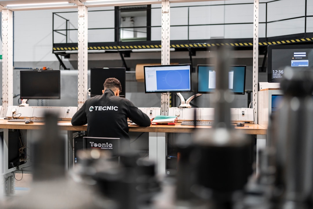 why-choose-us-03 Technician working on the design or analysis of mechanical components in front of several monitors at a computer station within an industrial plant.